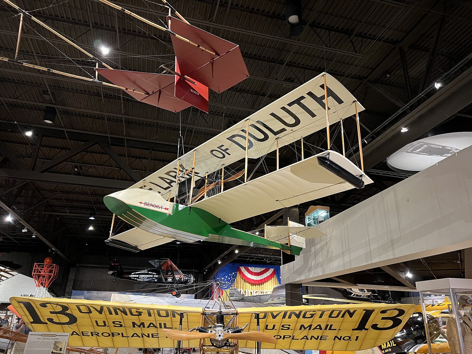 A replica of a green-and-white Benoist XIV flying boat hanging from the ceiling of an aviation museum
