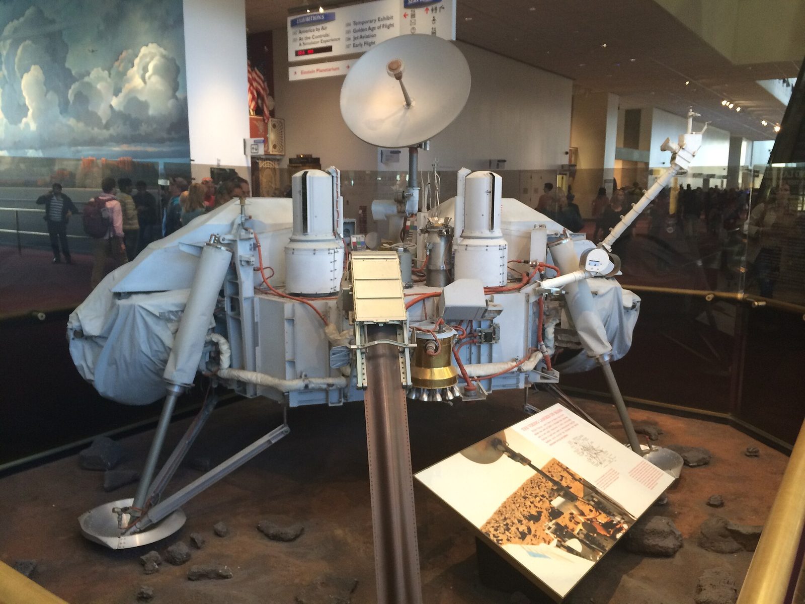 A full-size Mars lander spacecraft on display behind glass at the National Air and Space Museum, with visitors walking in the hall behind it