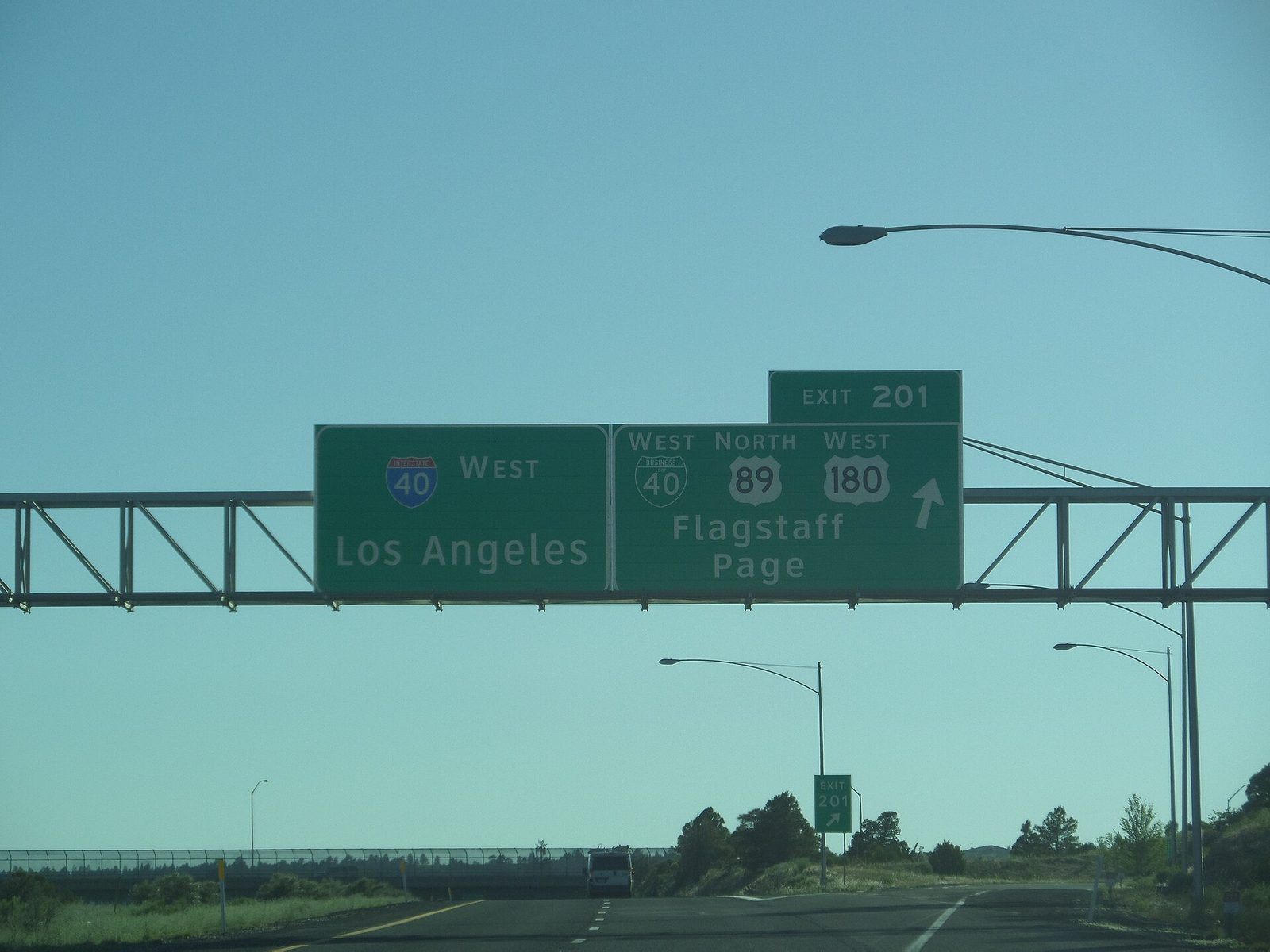 A green overhead interstate sign for I-40 West to Los Angeles and Exit 201 to Flagstaff and Page, above an open highway under a clear sky