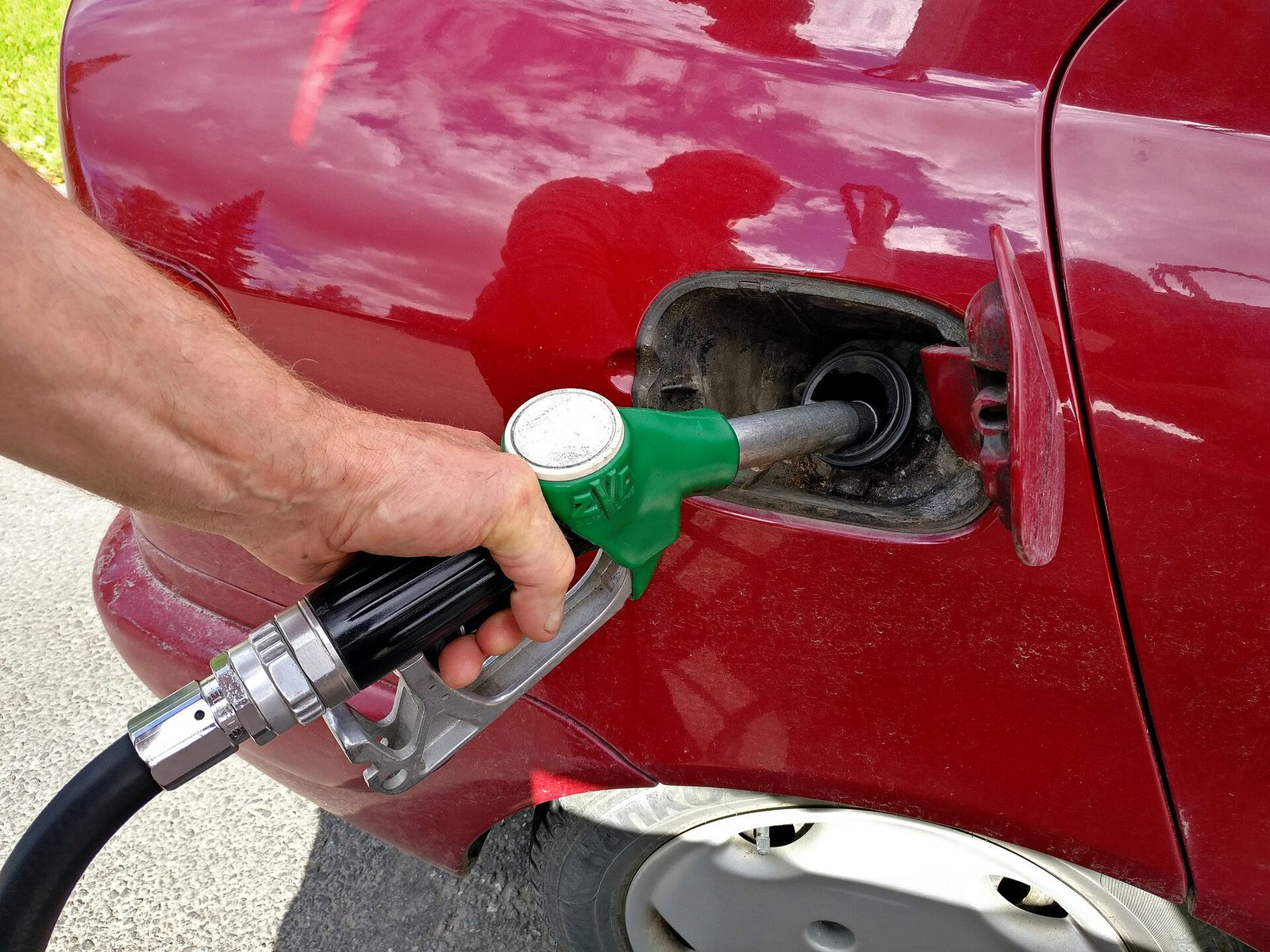 A hand holding a green gas pump nozzle in the open fuel door of a red car