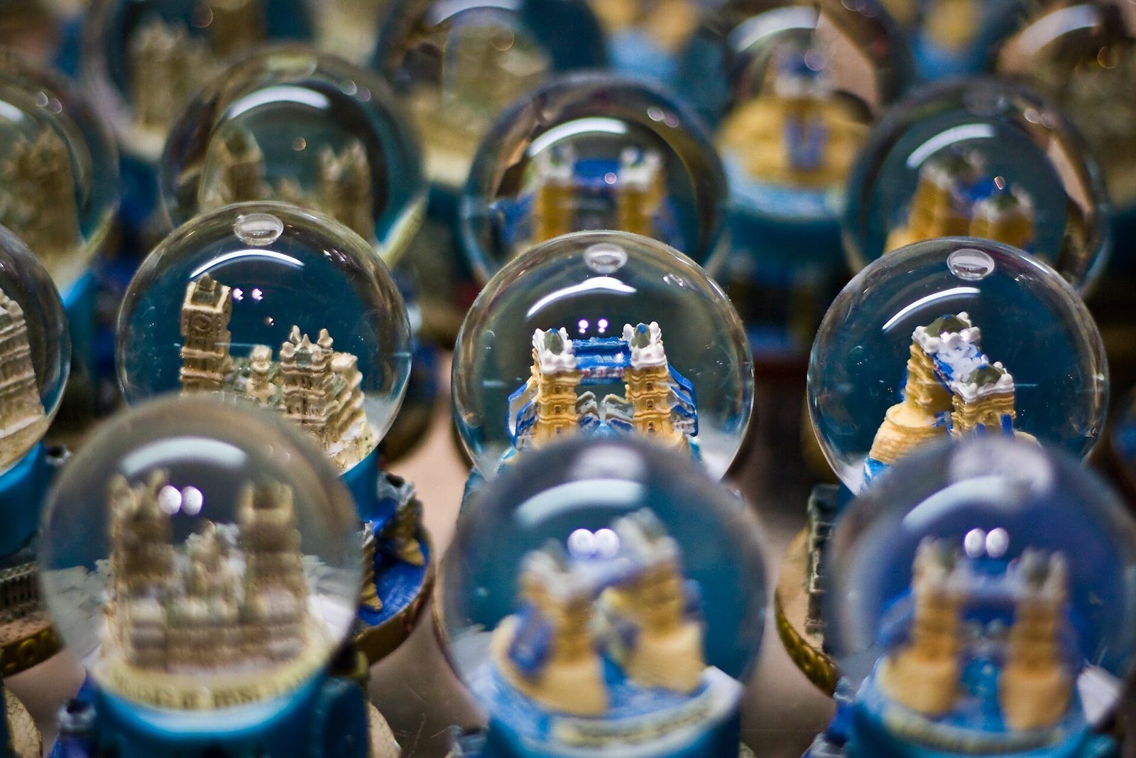 Rows of small souvenir snow globes with model buildings and bridges inside, shown in a close-up with a shallow focus