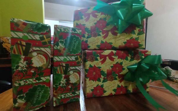 Four Christmas presents wrapped in red, green and gold holiday paper with green ribbon bows, stacked on a wooden table