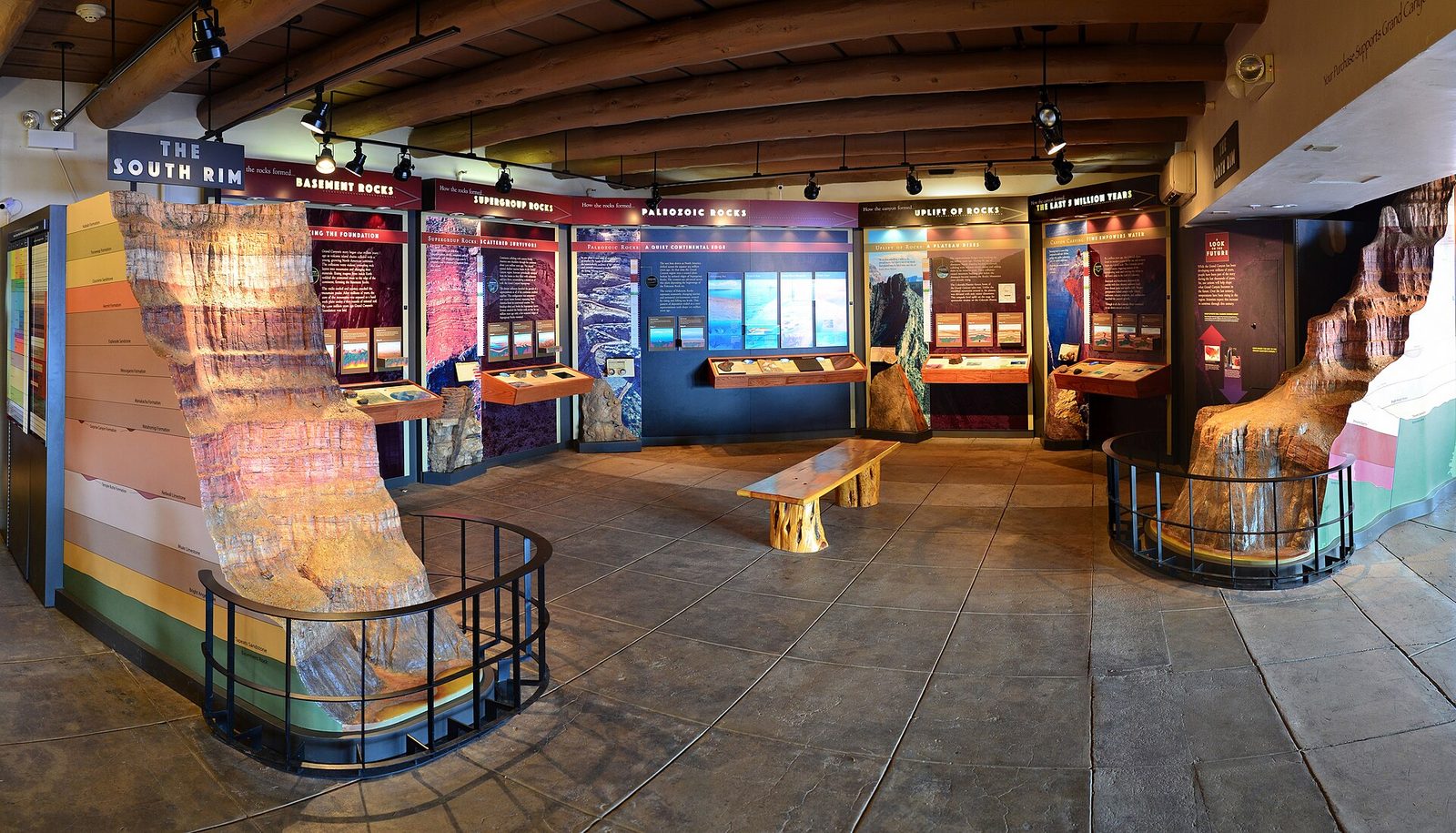 The inside of the Yavapai Geology Museum with large rock-layer models, colorful exhibit panels and a wooden bench