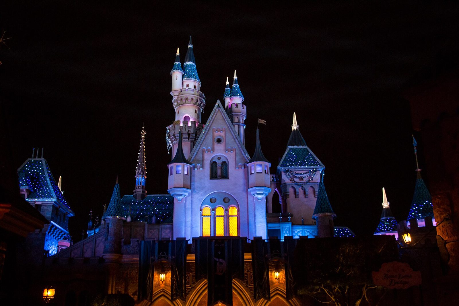 Sleeping Beauty Castle at Disneyland at night, lit in blue and purple with sparkling white lights on its roofs and towers