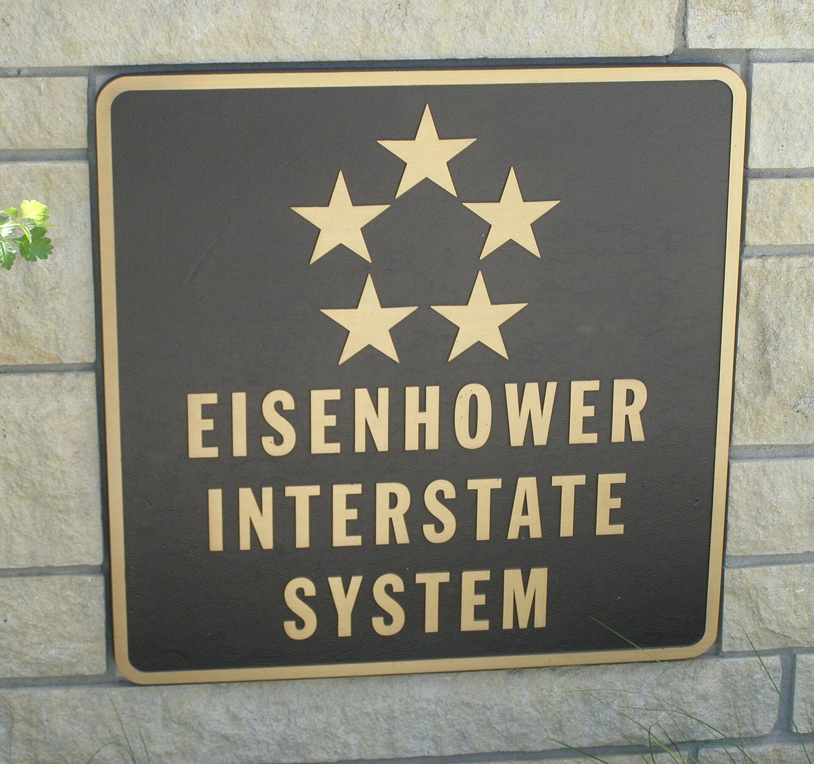 A bronze-colored plaque with five gold stars arranged in a circle above the words Eisenhower Interstate System, mounted on a stone wall