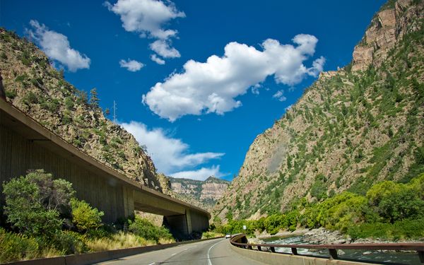 Interstate 70 winding through Glenwood Canyon in Colorado, with an elevated roadway along steep green canyon walls and the Colorado River beside the road