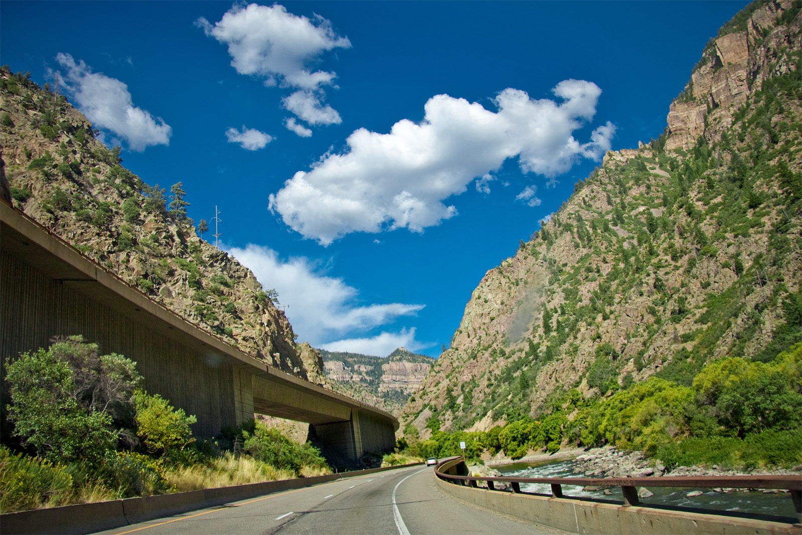 Interstate 70 winding through Glenwood Canyon in Colorado, with an elevated roadway along steep green canyon walls and the Colorado River beside the road