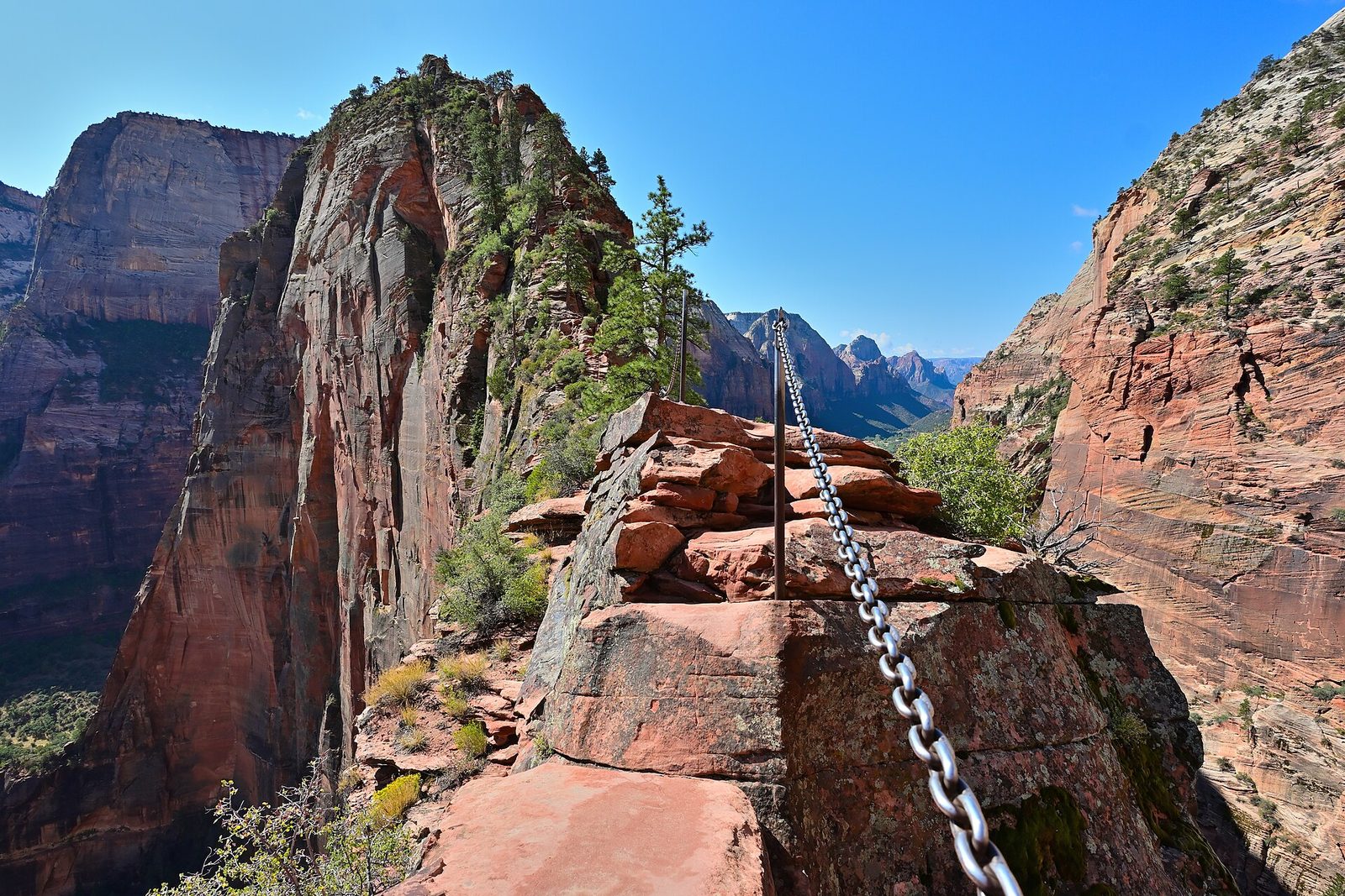 The chain-lined section of the Angels Landing Trail on a sandstone ridge above Zion Canyon under a blue sky