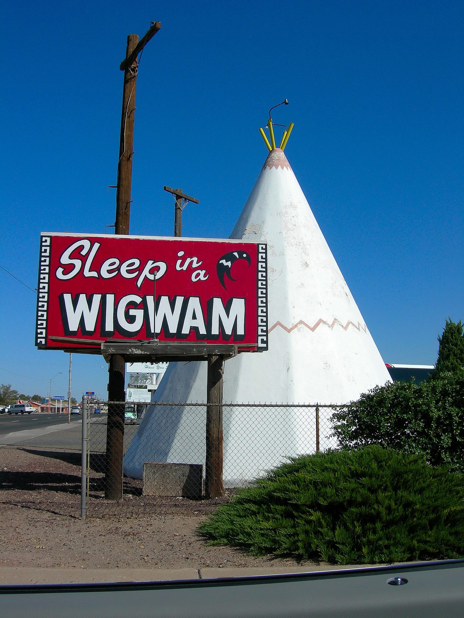 A red "Sleep in a Wigwam" sign in front of a tall white concrete teepee at a roadside motel