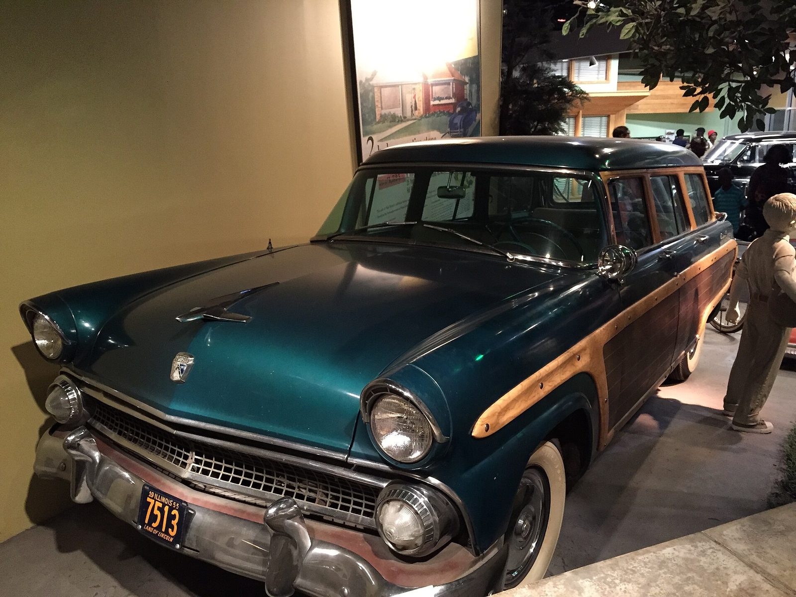 A teal 1955 Ford Country Squire station wagon with wood-grain side panels on display in a museum