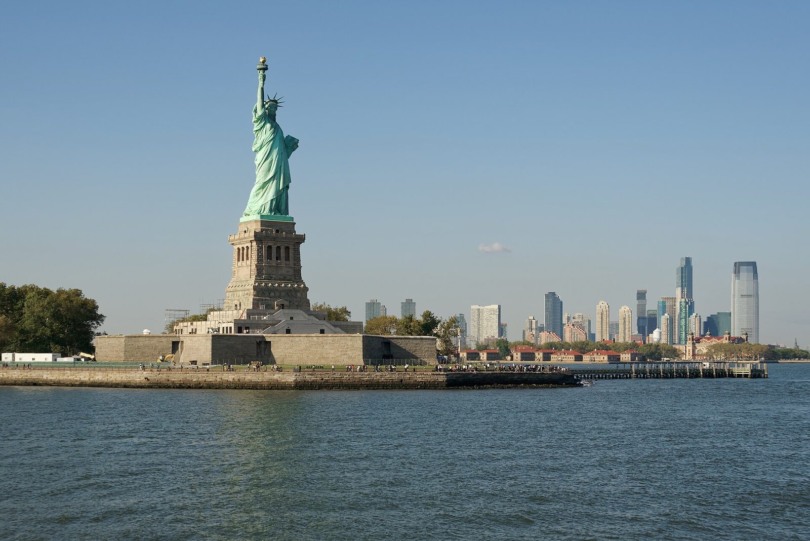 The Statue of Liberty on Liberty Island seen from the ferry on a clear day, with Ellis Island and the Jersey City skyline to the right