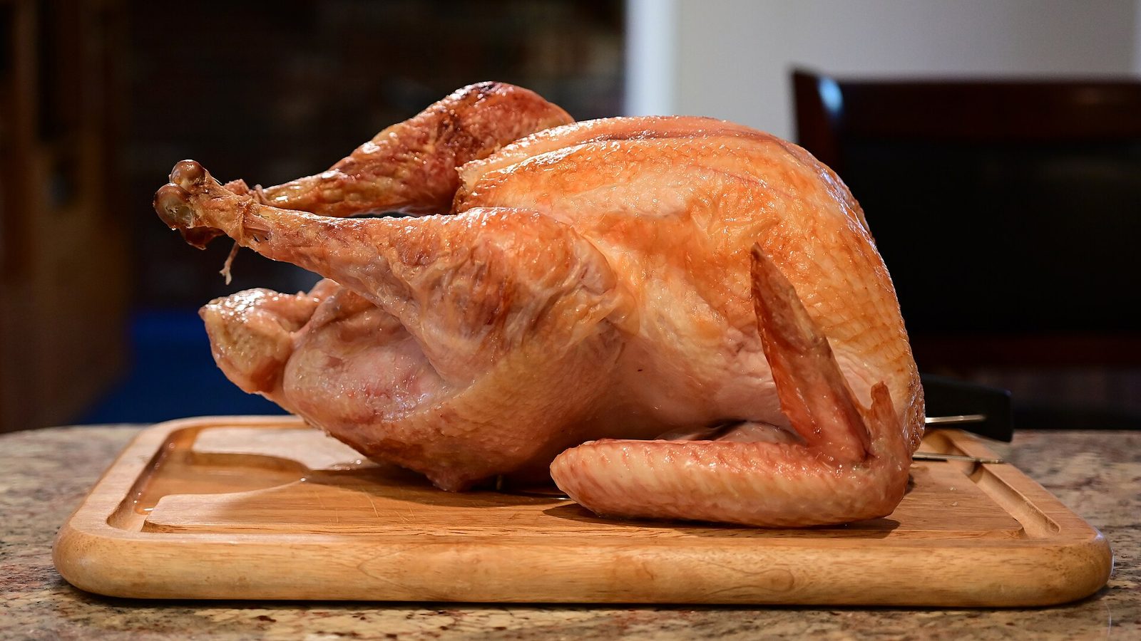 A whole roasted turkey on a wooden carving board on a granite kitchen counter