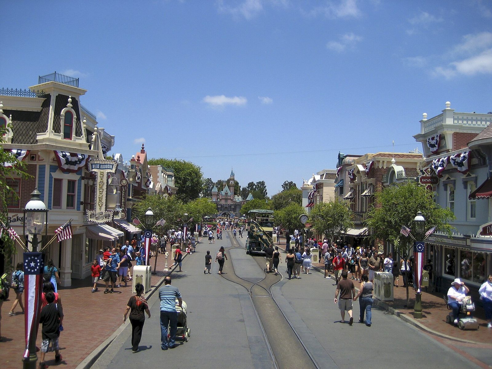 Main Street, U.S.A. at Disneyland decorated with red, white and blue bunting, with families and strollers walking toward Sleeping Beauty Castle in the distance