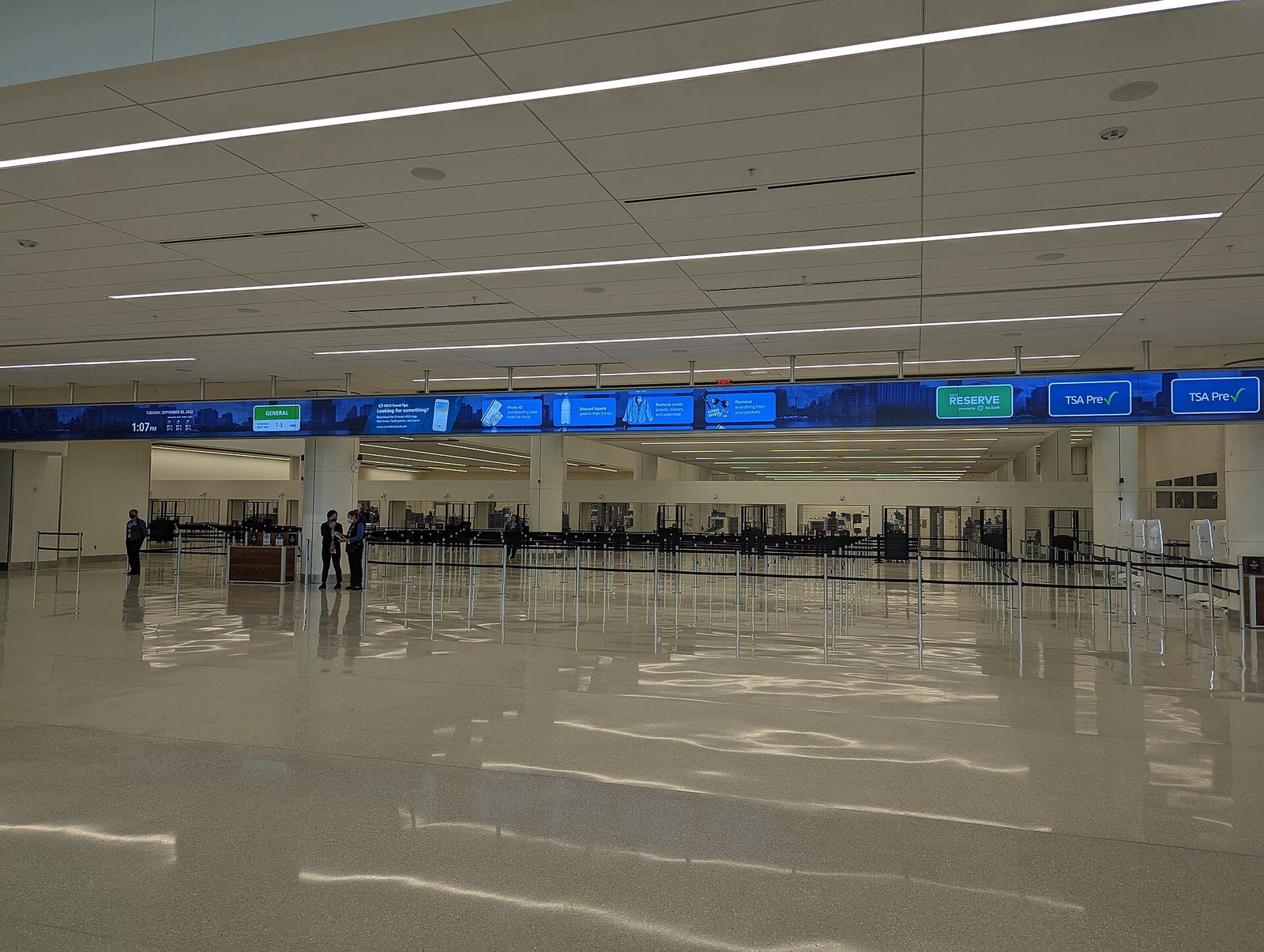 A wide, nearly empty security checkpoint at Orlando International Airport's Terminal C, with a long digital sign showing General, Reserve and TSA PreCheck lane labels