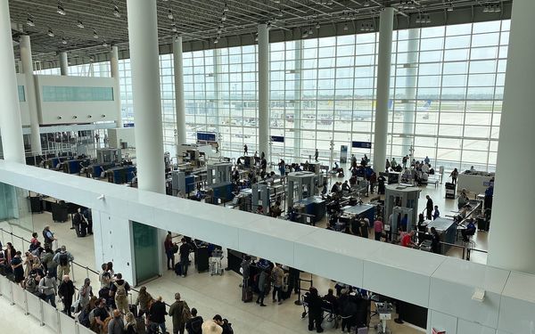 View from a balcony over a busy TSA security checkpoint at New Orleans airport, with travellers queuing and screening lanes in front of tall windows
