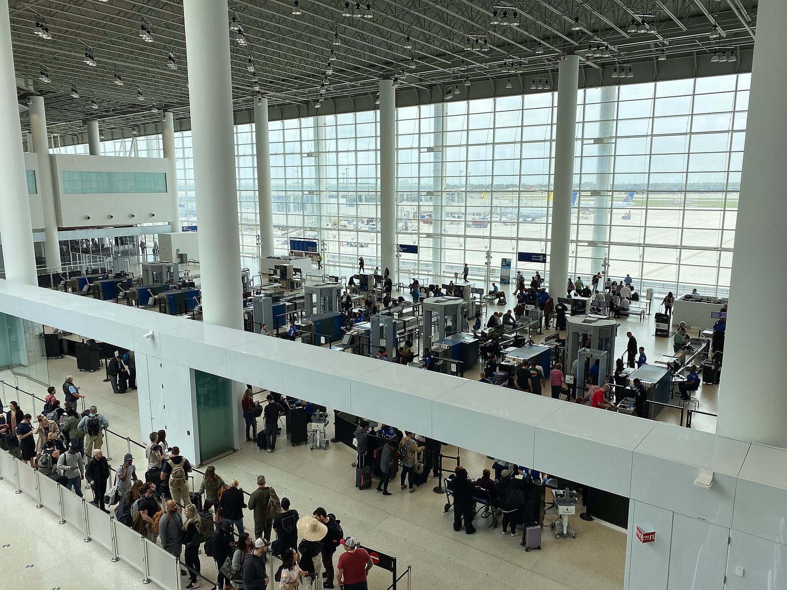 View from a balcony over a busy TSA security checkpoint at New Orleans airport, with travellers queuing and screening lanes in front of tall windows