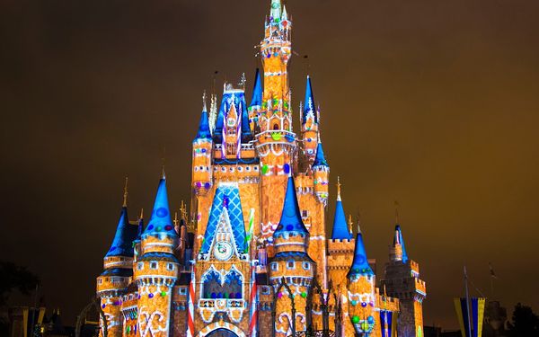 Cinderella Castle at Magic Kingdom at night, lit with colorful holiday projections in orange, blue and white