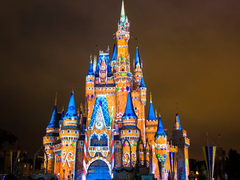 Cinderella Castle at Magic Kingdom at night, lit with colorful holiday projections in orange, blue and white